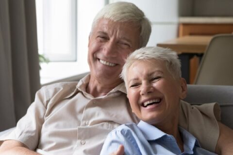 A smiling senior couple has a sweet moment together on a couch.
