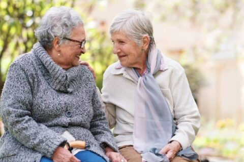 Two senior women sitting together on a bench outside.